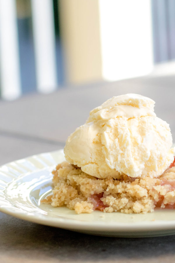 cobbler Peach cobbler on a green plate with vanilla bean ice cream on top outside on a patio table.
