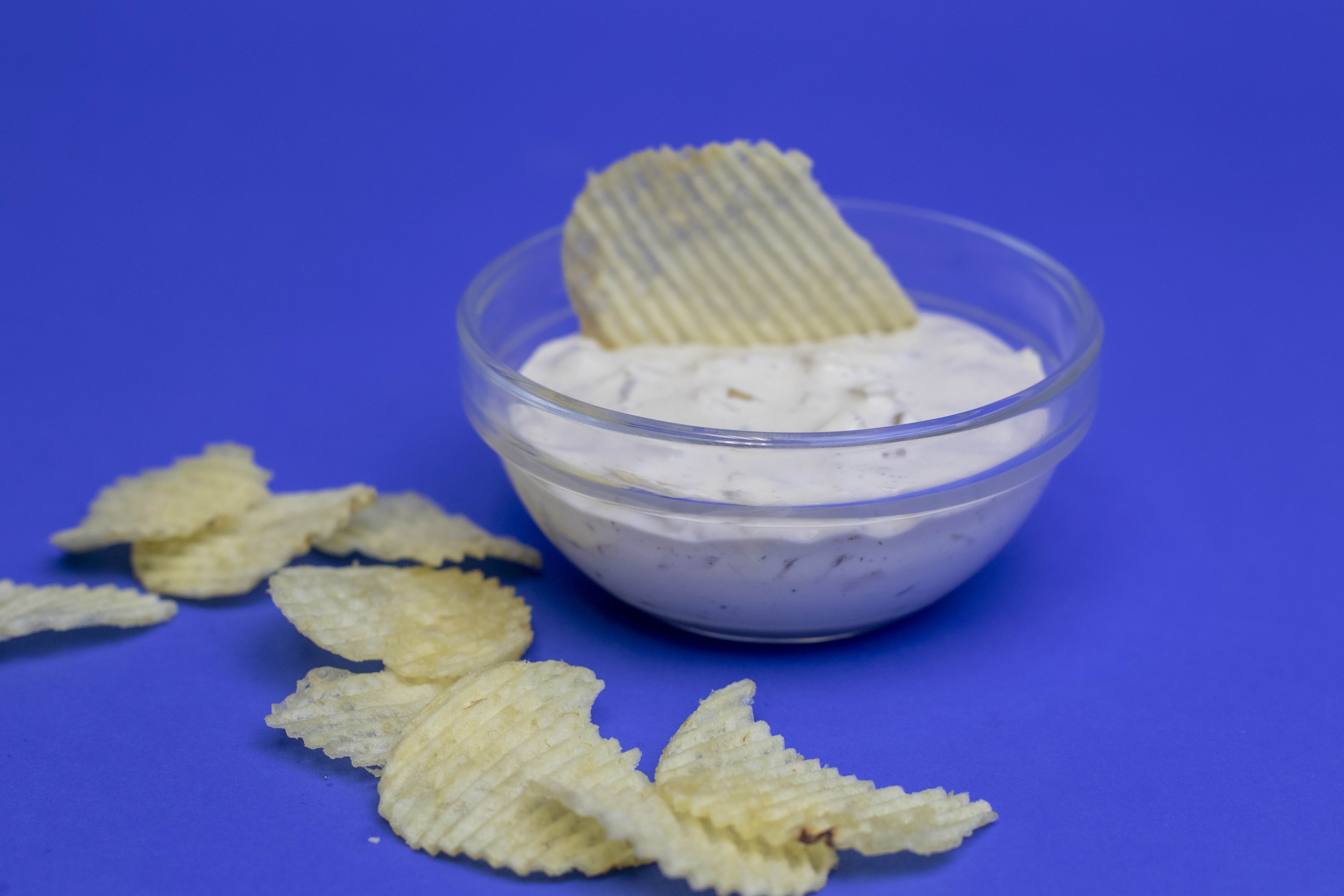 ribbed potato chip in a clear bowl of homemade onion dip on a blue backdrop