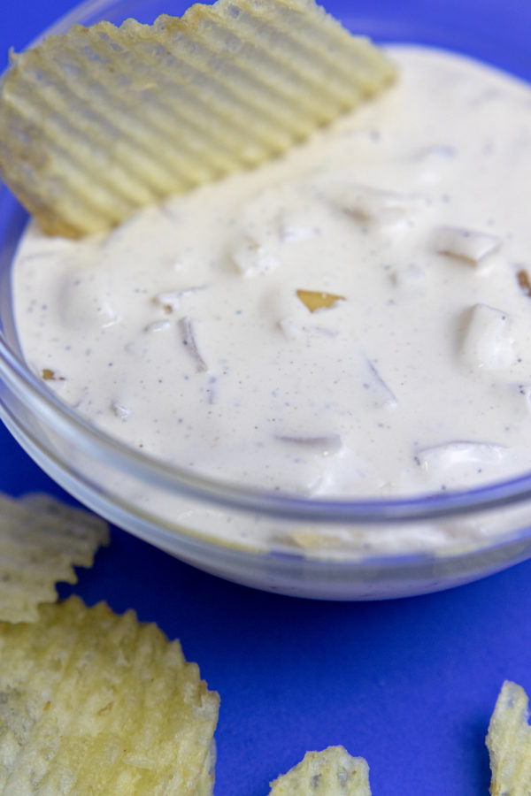 oniondip5 ribbed potato chip in a clear bowl of homemade onion dip on a blue backdrop
