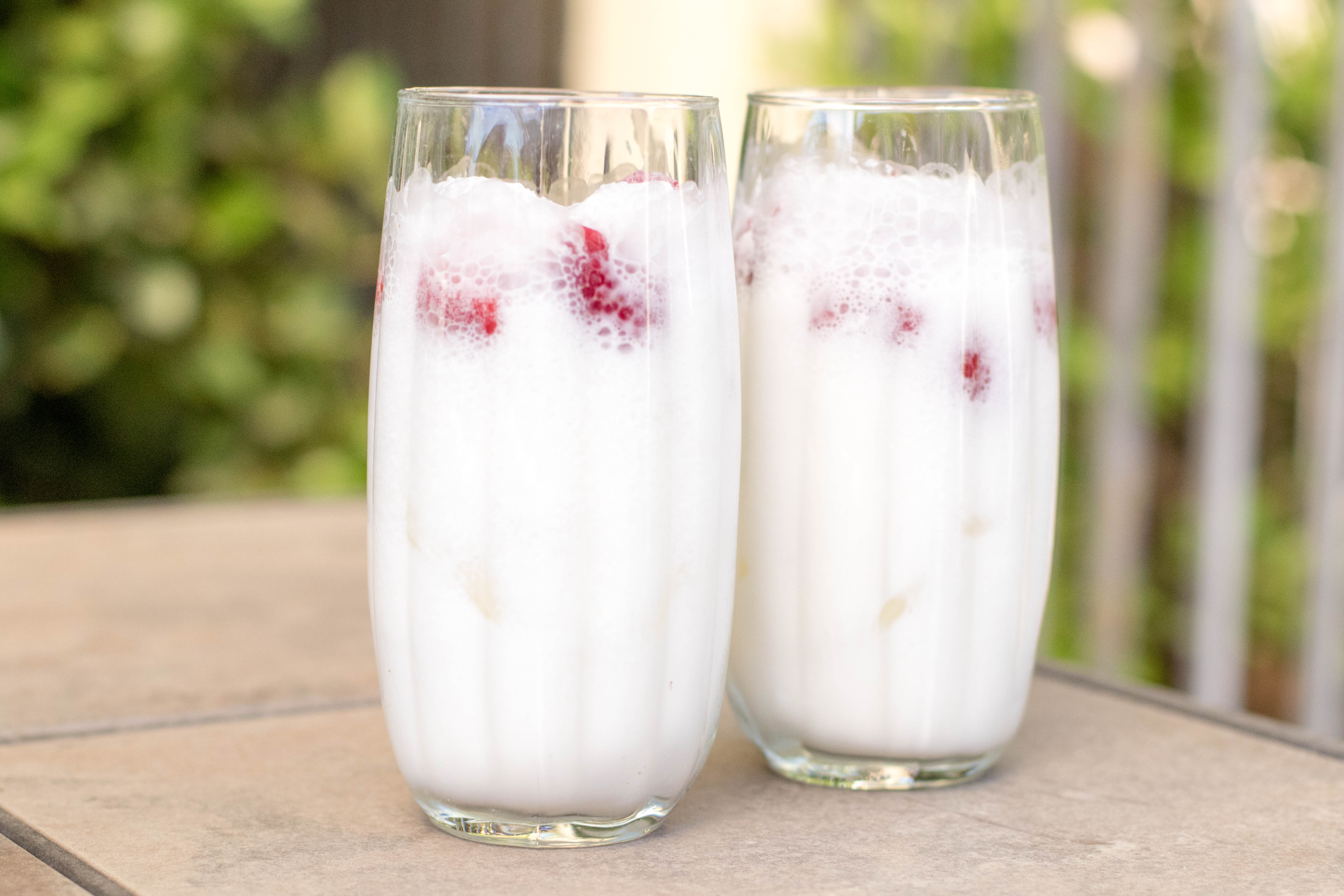 Raspberry and cream Italian soda in a clear cup outside on a patio table.