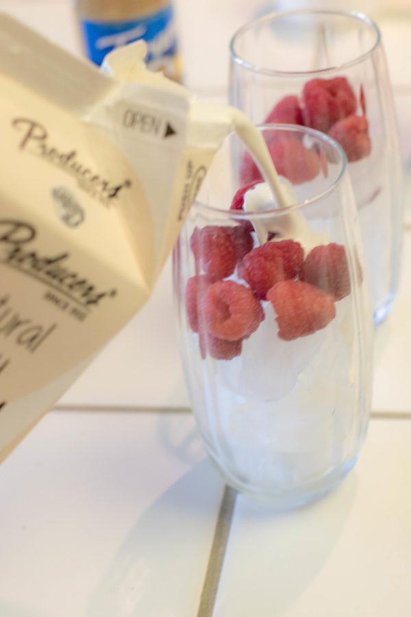 recipe2 (1 of 1) Natural Cream being poured into a clear glass with ice and raspberries on a kitchen counter.