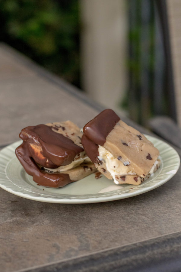 recipe2 (1 of 1) cookie dough ice cream sandwiches coated in chocolate on a green plate sitting on a patio table outside.