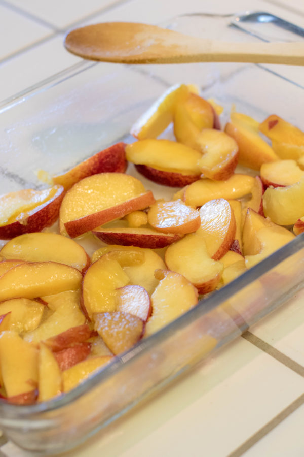recipe3 (1 of 1) sliced peaches coated in sugar in a baking dish with a wooden spoon to mix it with.