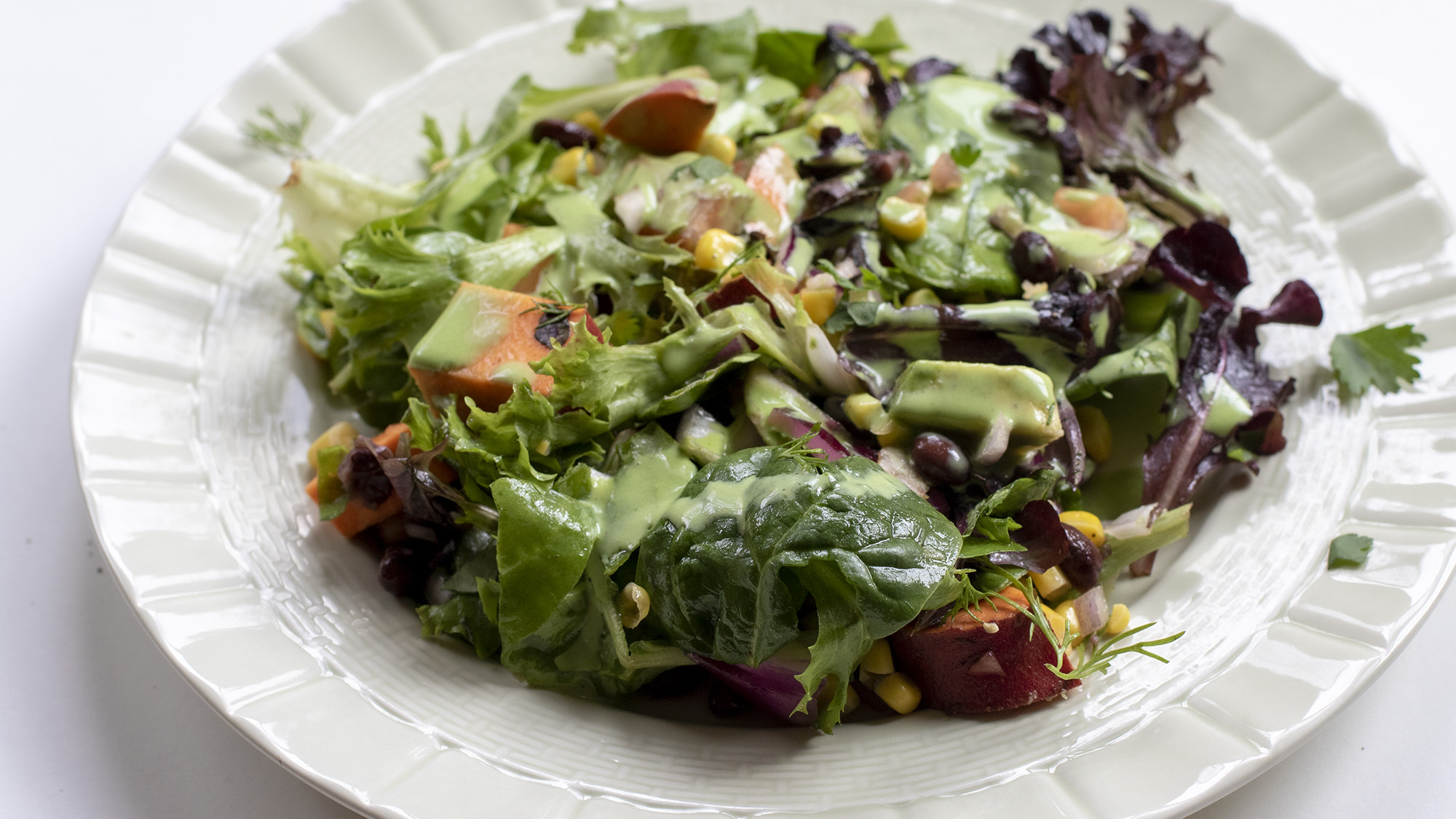 Southwestern salad with dressing on a green plate on a white background.